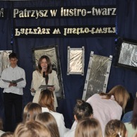 Scena z kobietą i chłopakiem przed publicznością, w tle lustrzane dekoracje i hasło „Patrzysz w lustro – twarz”.