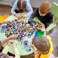 Zdjęcie nr 7 przedstawia dzieci siedzące  przy okrągłym, zielonym stole. Na stole są rozsypane klocki LEGO.